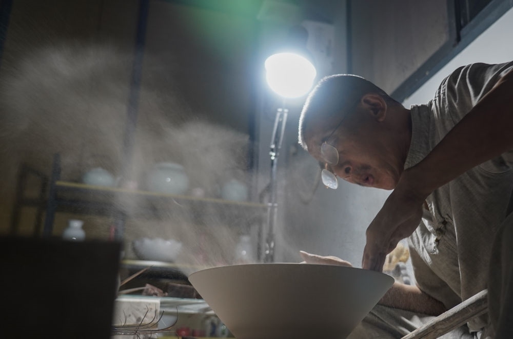 ↑ 在景德鎮(zhèn)，手工匠人吹去坯內(nèi)的泥土（2021年7月14日攝）。