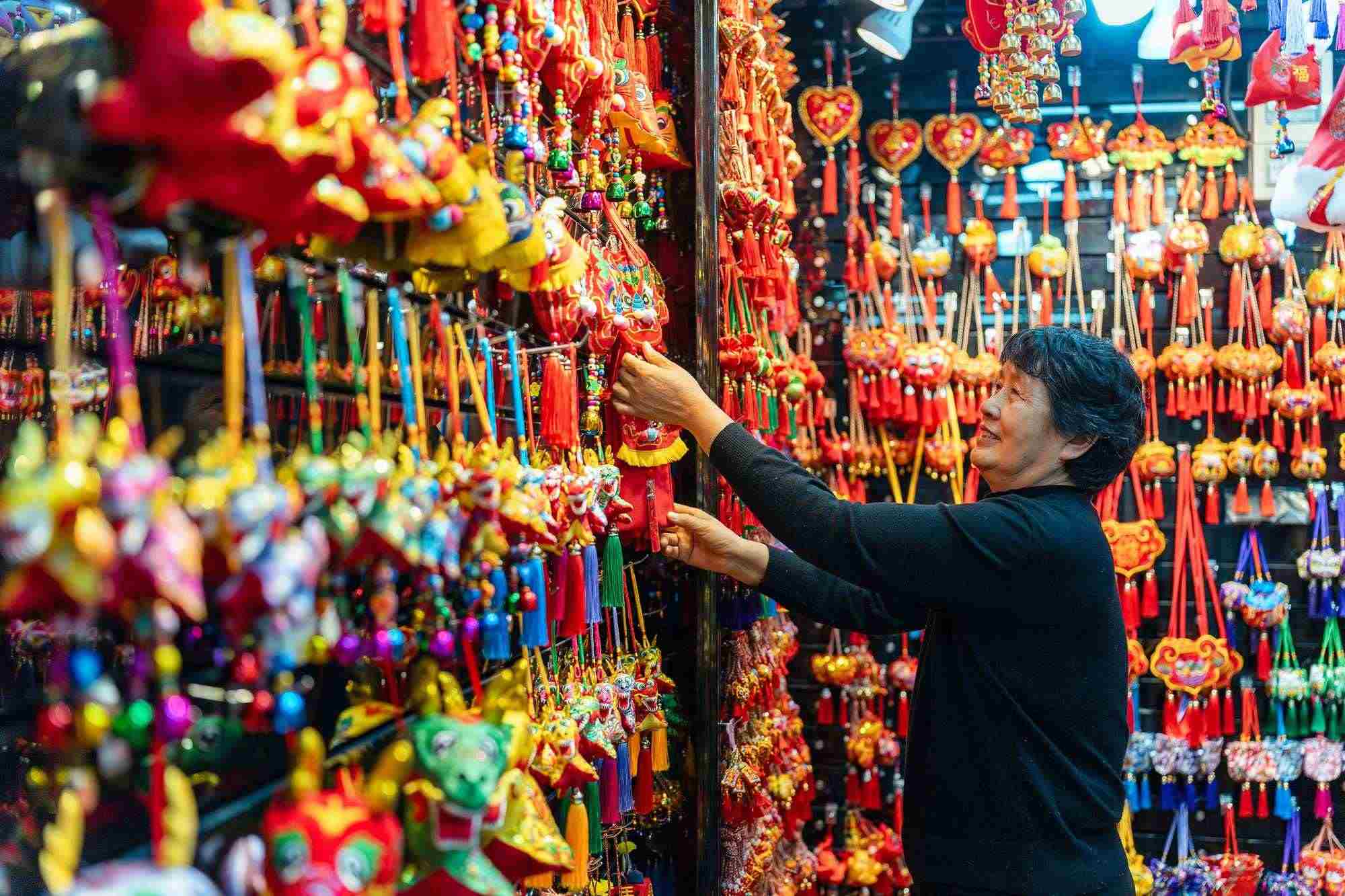 2023年12月11日，金華義烏國(guó)際商貿(mào)城，龍年喜慶用品掛滿攤位，顧客正在挑選中。