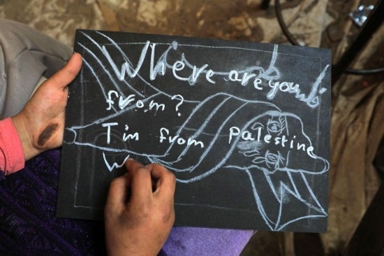 2023年12月28日，一名學(xué)生在加沙地帶南部城市拉法一所學(xué)校的臨時教室中寫下“我來自巴勒斯坦”的字樣。新華社發(fā)（里澤克·阿卜杜勒賈瓦德攝）