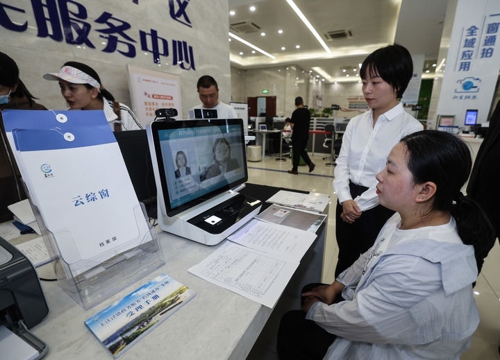 在浙江省嘉興市秀洲區(qū)王江涇鎮(zhèn)便民服務(wù)中心的“跨域通辦·云綜窗”窗口，辦理開業(yè)登記的個體工商戶（右一）通過該系統(tǒng)與江蘇省蘇州市吳江區(qū)盛澤鎮(zhèn)行政審批局工作人員視頻連線，進行身份讀取及材料線上審核（2024年5月9日攝）。新華社記者 徐昱 攝