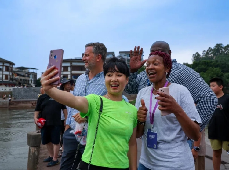 2024“一帶一路”媒體合作論壇聯(lián)合采訪調(diào)研行成員在樂(lè)山蘇稽古鎮(zhèn)與游客合影留念。本報(bào)記者 伊霄攝