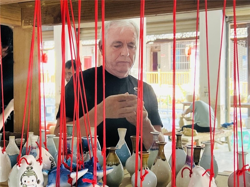 鄉(xiāng)愁如同一根根紅線，將游子與故鄉(xiāng)永遠(yuǎn)地牽連到一起?；逄账囄幕瘎?chuàng)意一條街的母氏陶藝館內(nèi)，紅線吊著陶瓶，思緒游走萬里。摩爾多瓦“信息標(biāo)簽”通訊社社長亞歷山大·塔納斯端詳著館內(nèi)展示的陶藝作品，并挑選出心儀的小擺件帶回摩爾多瓦，也帶走花茂村的“鄉(xiāng)愁”。（張亞欣攝）