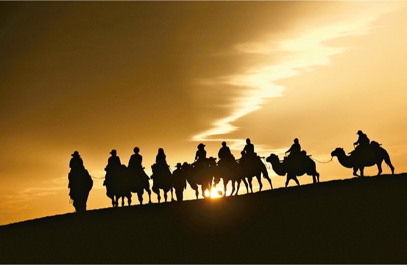 新時(shí)代以來，文化和旅游深度融合發(fā)展體制機(jī)制不斷健全，成功走出了一條獨(dú)具特色的中國(guó)旅游發(fā)展之路。圖為2024年9月1日清晨，游客在甘肅省敦煌市鳴沙山月牙泉景區(qū)乘騎駱駝，欣賞大漠風(fēng)光，體驗(yàn)絲路風(fēng)情。 新華社發(fā) 張曉亮/攝