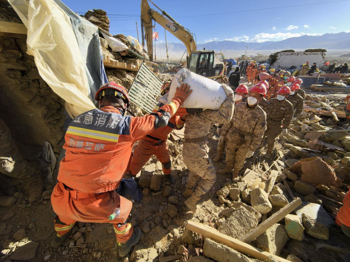 1月11日，定日縣長所鄉(xiāng)古榮村，應急消防等救援人員排隊接力搶運掩埋在倒塌房屋下的群眾財物。人民日報記者楊翹楚攝