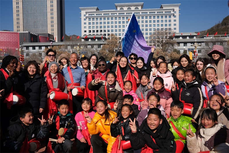 中外青年學(xué)子在安塞文化廣場(chǎng)觀看陜北腰鼓和大秧歌表演后合影留念，大家踏著鼓點(diǎn)共舞，翻飛的紅綢與躍動(dòng)的身影交織，在黃土地廣場(chǎng)上繪出一幅生動(dòng)的陜北民俗互動(dòng)畫(huà)卷